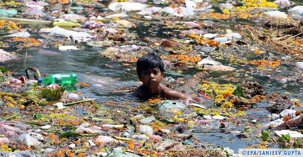 Bambino nuota nel lago di Jawahar (India) coperto di rifiuti, 2014 